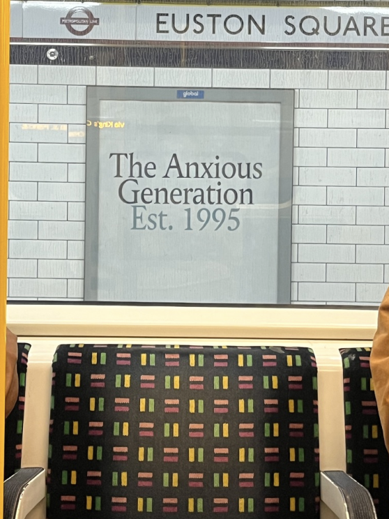 A poster on a London Underground platform reading The Anxious Generation, Est. 1995, seen above patterned Tube seats